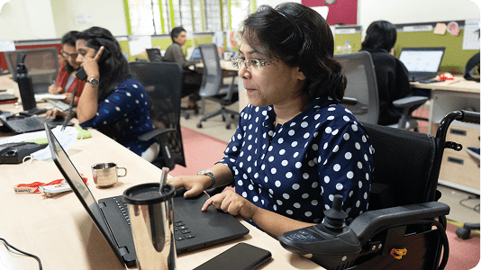 Woman in wheelchair working on laptop in inclusive office.
