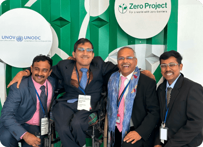 Four men in formal attire smiling and posing together at the Zero Project event, with banners of UNODC and Zero Project in the background.