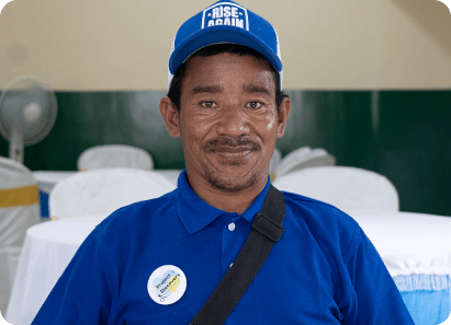 Man in a blue shirt and cap smiling at the camera, wearing a badge